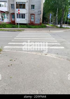 Fußgängerüberquerung durch die Straße. Weiße, schäbige, alte Streifen auf dem Asphalt. Das Konzept des Verkehrs, der städtischen Umwelt, des Straßenverkehrs und der Sicherheit. Stockfoto