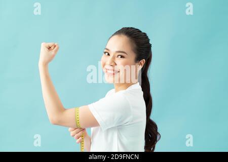 Frau misst ihr überschüssiges Arm Fett durch gelbe Maßband auf isoliertem Hintergrund. Stockfoto