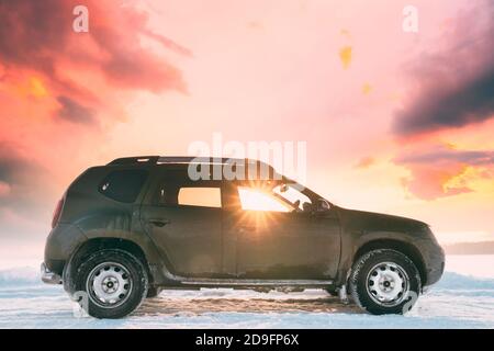 Sonnenstrahlen durch das Fenster des SUV-Autos geparkt auf Winter Snowy Field bei Sunset Dawn Sonnenaufgang. Veränderter Sonnenuntergang Himmel Stockfoto