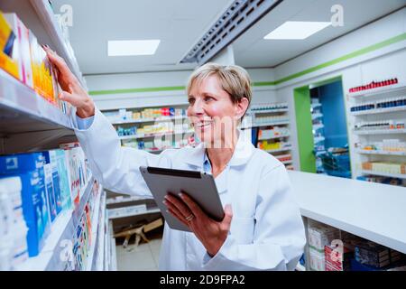 Kaukasische leitende Apotheker hält digitale Tablette Überprüfung Mediation in den Regalen In der Apotheke Stockfoto
