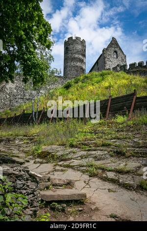 Bezdez, Tschechische Republik - Juli 19 2020: Turm und ein Haus, Teil der mittelalterlichen Burg aus grauen Steinen auf einem steilen Hügel. Sonniger Tag, blauer Himmel. Stockfoto