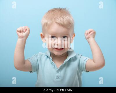 Ein drei-jähriger Junge hob seine Fäuste überrascht. Emotionen der Kinder. Kind auf blauem Hintergrund Stockfoto