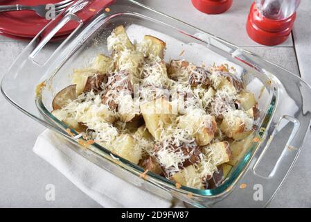 Geriebener Käse, der auf gebackenen Kartoffelwürfeln in einer Auflaufform geschmolzen wird. Stockfoto