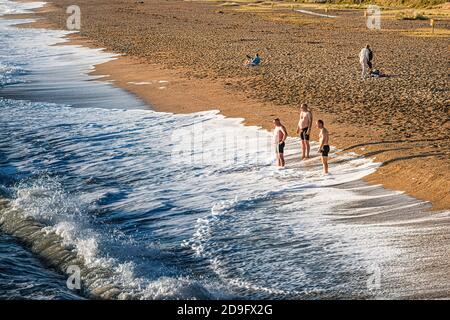 Alltag. Eine Gruppe von Männern beobachtete die Wellen am Strand an einem sonnigen, aber kalten Tag. Stockfoto
