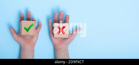 Nahaufnahme einer Hand, die zwei Holzklötze auf einem blauen Hintergrund platziert. True und false Symbole akzeptieren zur Auswertung abgelehnt, Ja oder Nein auf Holzblöcken ein Stockfoto