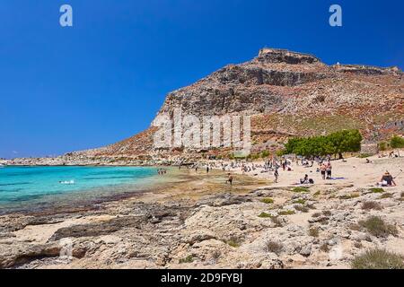 2019, 4. JUNI: - GRIECHENLAND, DIE INSEL KRETA, BALOS - die Burg auf dem Gipfel des Berges und die Menschen am Strand darunter. Stockfoto