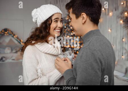 Glückliches junges Paar mit Weihnachtsgeschenken suchen einander genießen Familie gemütliche Momente drinnen während der Neujahrsferien, Spaß zusammen in gemütlichen Raum mit Weihnachtsbaum Stockfoto