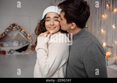 Junge Kerl küssen ihre schöne Freundin Gefühl Glück während der Feier Winterferien zusammen, romantisches Paar umarmt in der Nähe geschmückt weihnachtsbaum in gemütlichen Zuhause genießen Ferien Stockfoto