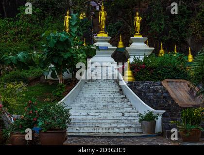 Krabi, Thailand- März 29 2019: Tiger Tempel dekorative weiße Felstreppe, Gold budha Statuen, Gartenblumen Stockfoto