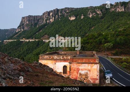 Haus des Straßenarbeiters an einer Bergstraße in Sardinien, Italien. Kleine Auto parkes auf der Seite. Regnerischer Tag am Abend Stockfoto