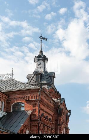 Fragment des oberen Teils des historischen Gebäudes mit einem Turm zeigt die Schönheit der Backsteinsakralen Architektur. Metall-Wetterfahne auf dem Dach von Stockfoto