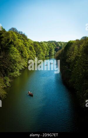 Ein paar Boote entlang eines angenehmen Flusses. Flankiert von dicken grünen Bäumen und sonnen in einem Sommer Sonnen dösen Glanz sonnen. Ein einziges Boot in Richtung Vordergrund zieht. Stockfoto