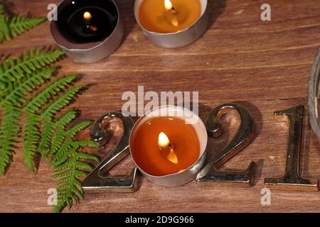 Brennende Kerzenfiguren 2021 und Farn auf Holzhintergrund. Stockfoto