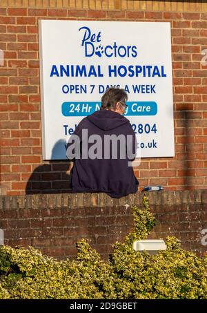Eine Frau, die außerhalb einer tierärztlichen Operation oder Tierklinik wartet, um von einem Tierarzt mit einem schlecht Tier, das Pflege oder Aufmerksamkeit benötigt, gesehen zu werden. Stockfoto