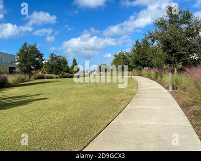 Ein wunderschön angelegter Gehweg in einer Nachbarschaft, gesäumt von Bäumen, Gras und Pampagras. Stockfoto