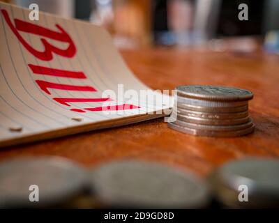 Münzstapel, Notizblock mit dem Wort Bill! Und ein Haufen Münzen im Vordergrund. Stockfoto