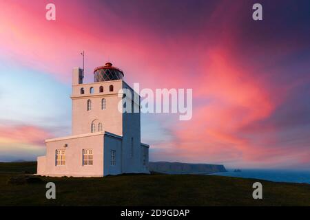 Unglaubliche Abendansicht des Dyrholaey Leuchtturms am Kap Dyrholaey, Südküste Islands. Große lila Sonnenuntergang leuchtet auf dem Hintergrund. Landschaftsfotografie Stockfoto