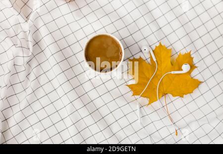 Herbstkomposition. Tasse kaffeetasse, Herbstblätter und Kopfhörer auf weißem kariertem Tuch. Flach liegend, Draufsicht, Kopierbereich Stockfoto