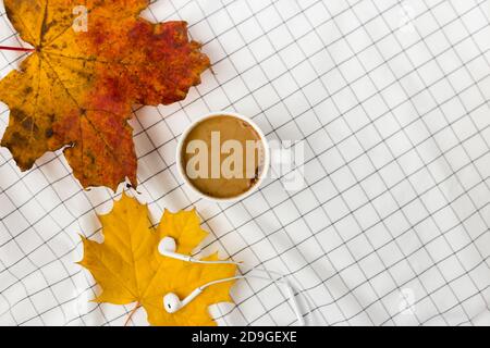 Herbstkomposition. Tasse kaffeetasse, Herbstblätter und Kopfhörer auf weißem kariertem Tuch. Flach liegend, Draufsicht, Kopierbereich Stockfoto