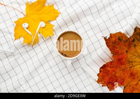 Herbstkomposition. Tasse kaffeetasse, Herbstblätter und Kopfhörer auf weißem kariertem Tuch. Flach liegend, Draufsicht, Kopierbereich Stockfoto