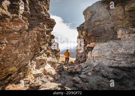 Mann, der auf einem Gipfel zwischen Felsen im Rocky steht Mountain National Park und mit Blick auf die Bergkette Ein kältiger und windiger Tag Stockfoto