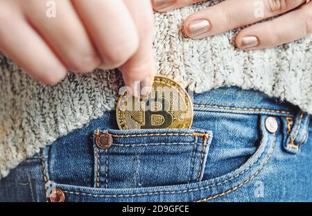 Nahaufnahme einer Frau, die eine einzelne Bitcoin in sie setzt Jeans-Tasche Stockfoto