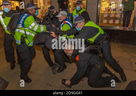 London, Großbritannien. November 2020. Polizeibeamte in gut sichtbarer und taktischer Ausrüstung halten maskierte Demonstranten während des Millionen-Maskenmarsches im Zentrum Londons fest. Die nächtliche Szene zeigt Einzelpersonen, die auf dem Bürgersteig festgehalten werden, wobei einer eine Kamera hält. Spannungen und Dringlichkeit sind in der Protestatmosphäre offensichtlich. Hunderte antikapitalistischer Demonstranten nehmen an der jährlich stattfindenden Mask March Demonstration im Zentrum Londons teil. Penelope Barritt/Alamy Live News Stockfoto