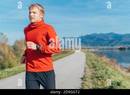 Ein Mann in roten Langarmshirt haben einen Morgen Joggen durch die Straße mit einem Berg Hintergrund gekleidet. Sportliche Aktivitäten und ein gesunder Lebensstil Stockfoto
