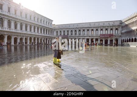 Touristen fotografieren auf dem Markusplatz bei Flut, Acqua alta, mit Blick auf die San Marco Procuratie Stockfoto