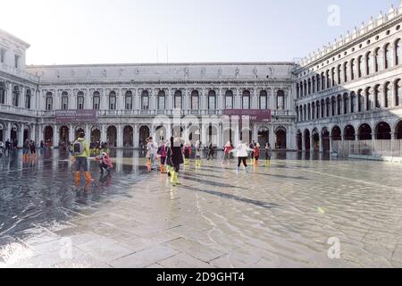 Touristen fotografieren auf dem Markusplatz bei Flut, Acqua alta, mit Blick auf die San Marco Procuratie Stockfoto