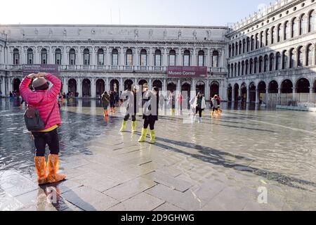 Touristen fotografieren auf dem Markusplatz bei Flut, Acqua alta, mit Blick auf die San Marco Procuratie Stockfoto