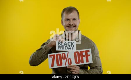 Schockiert erstaunt Emotionen des Store-Kunden. Mann zeigt Black Friday und bis zu 70 Prozent aus Inschriften Zeichen. Gute Urlaubsrabatte, niedrige Preise zum Einkaufen. Gelber Hintergrund Stockfoto