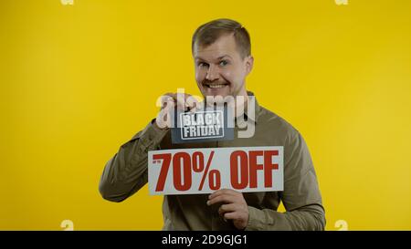 Schockiert erstaunt Emotionen des Store-Kunden. Mann zeigt Black Friday und bis zu 70 Prozent aus Inschriften Zeichen. Gute Urlaubsrabatte, niedrige Preise zum Einkaufen. Gelber Hintergrund Stockfoto