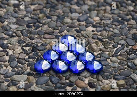 Dreieck von schillernden blauen Glasperlen auf einem Kieselgestein Hintergrund isoliert. Stockfoto