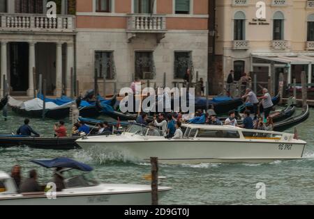 Ein Boot führt ausländische Touristen an anderen Booten und Gondeln vorbei, die Touristen auf dem überfüllten Granalkanal in Venedig, Italien, befördern. Stockfoto