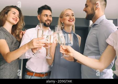 Junge Leute klirren Gläser mit leckeren Champagner bei Party in Büro Stockfoto