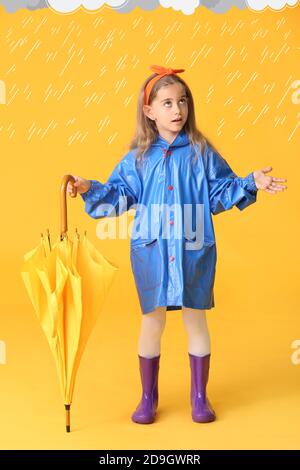 Nettes kleines Mädchen in Regenmantel und mit Regenschirm unter gezeichnet Regentropfen auf farbigem Hintergrund Stockfoto