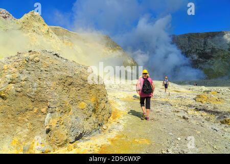 Touristen wandern durch die Landschaft von White Island, einem aktiven Vulkan in der Bay of Plenty, Neuseeland, in Richtung des dampfenden Kratersees Stockfoto