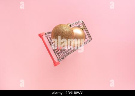 Einkaufswagen auf rosa Hintergrund mit goldenen weihnachtskugeln, Kugeln. Frohe Weihnachten und glückliches neues Jahr Kauf online oder Verkauf Konzept. Stockfoto