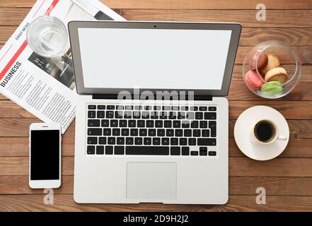 Moderner Laptop mit Handy und Tasse Kaffee an Holzhintergrund Stockfoto