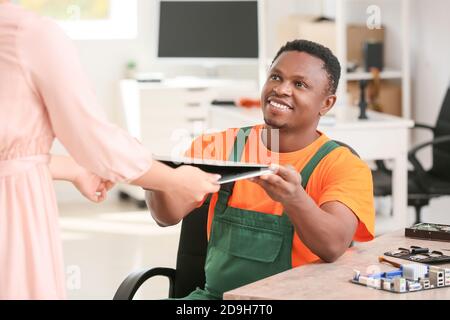 Afroamerikanischer Techniker, der dem Besitzer im Servicecenter einen festen Laptop übergibt Stockfoto