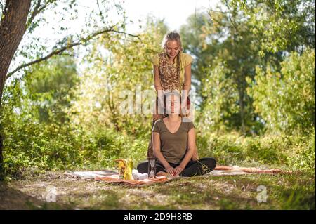 Heilerin wendet ihre Massagefähigkeiten auf ihren Klienten auf dem Gras des Waldes an. Stockfoto
