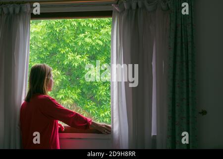 Frau von hinten Blick aus einem Fenster, mit einem Hintergrund aus grünen Blättern Stockfoto