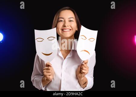 Junge talentierte Schauspielerin mit verschiedenen Masken auf dunklem Hintergrund Stockfoto