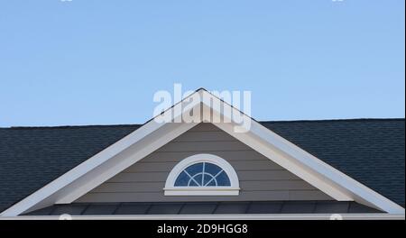 Einzel- und Doppelkiebel-Dächer mit Backstein- oder Vinylgleitviereck und ovalen Dachfenstern mit blauem, neutralem Himmel-Hintergrund Stockfoto