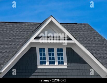 Einzel- und Doppelkiebel-Dächer mit Backstein- oder Vinylgleitviereck und ovalen Dachfenstern mit blauem, neutralem Himmel-Hintergrund Stockfoto