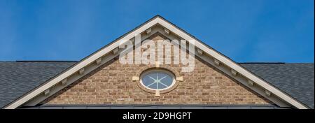 Einzel- und Doppelkiebel-Dächer mit Backstein- oder Vinylgleitviereck und ovalen Dachfenstern mit blauem, neutralem Himmel-Hintergrund Stockfoto