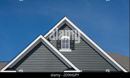 Einzel- und Doppelkiebel-Dächer mit Backstein- oder Vinylgleitviereck und ovalen Dachfenstern mit blauem, neutralem Himmel-Hintergrund Stockfoto