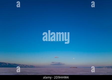 Fantastischer Sonnenuntergang mit Blick auf den Mond im Winter auf dem Eis des Baikalsees, Sibirien Russland. Natürliche Landschaft. Die Pracht der Natur. Speicherplatz kopieren. Stockfoto