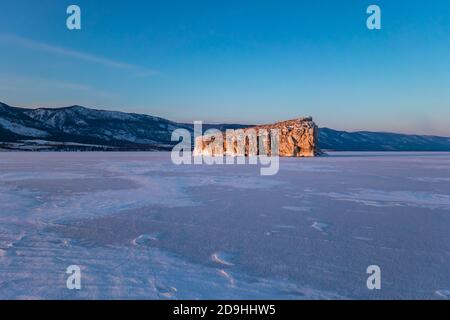 Fantastischer Sonnenuntergang mit Blick auf eine hell erleuchtete Insel im Winter auf dem Eis des Baikalsees, Sibirien Russland. Wintersaison Naturlandschaft. Speicherplatz kopieren. Stockfoto